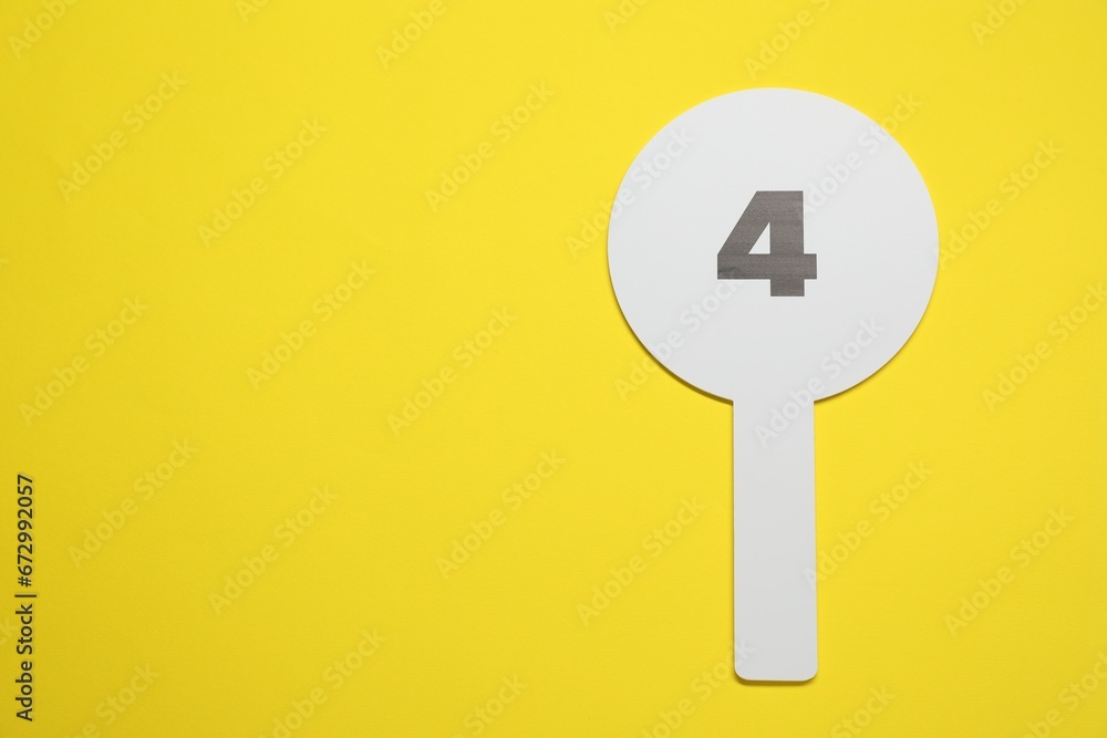 Auction paddle with number 4 on yellow background, top view. Space for text Auction paddle with number 4 on yellow background, top view. Space for text
