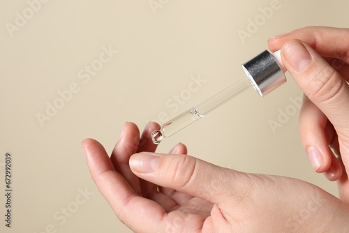 Woman applying cosmetic serum onto finger on beige background  closeup. Space for text