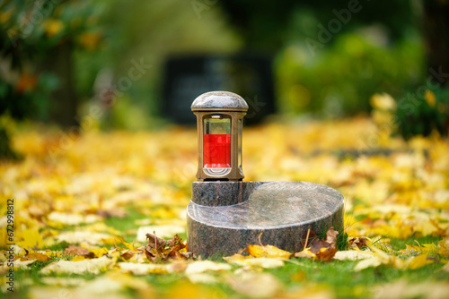grave lantern on an urn gravestone in a meadow covered with autumn leaves
