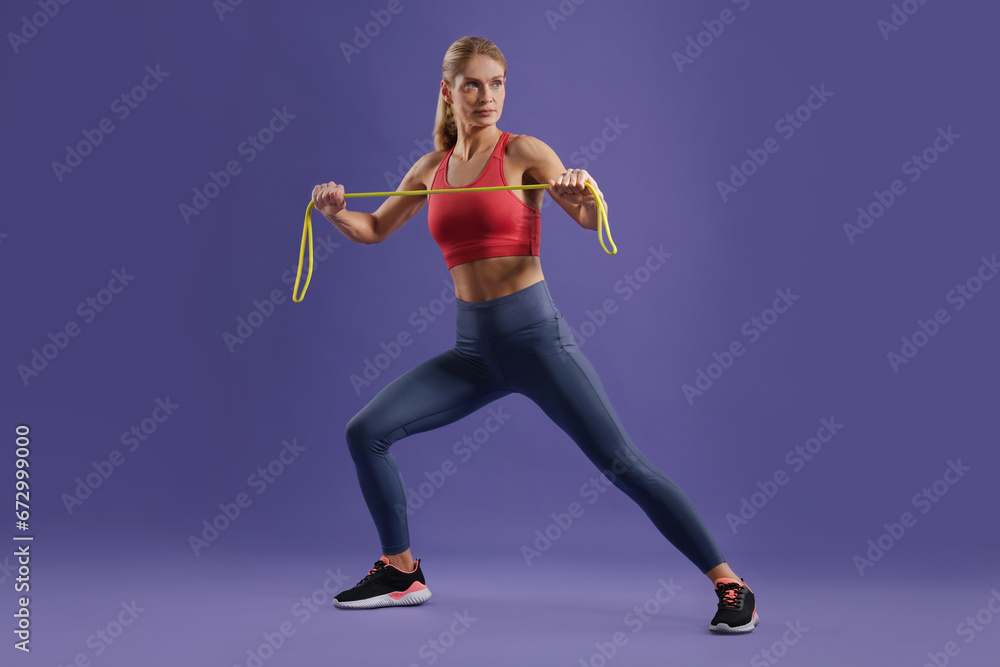 Fototapeta premium Athletic woman exercising with elastic resistance band on purple background