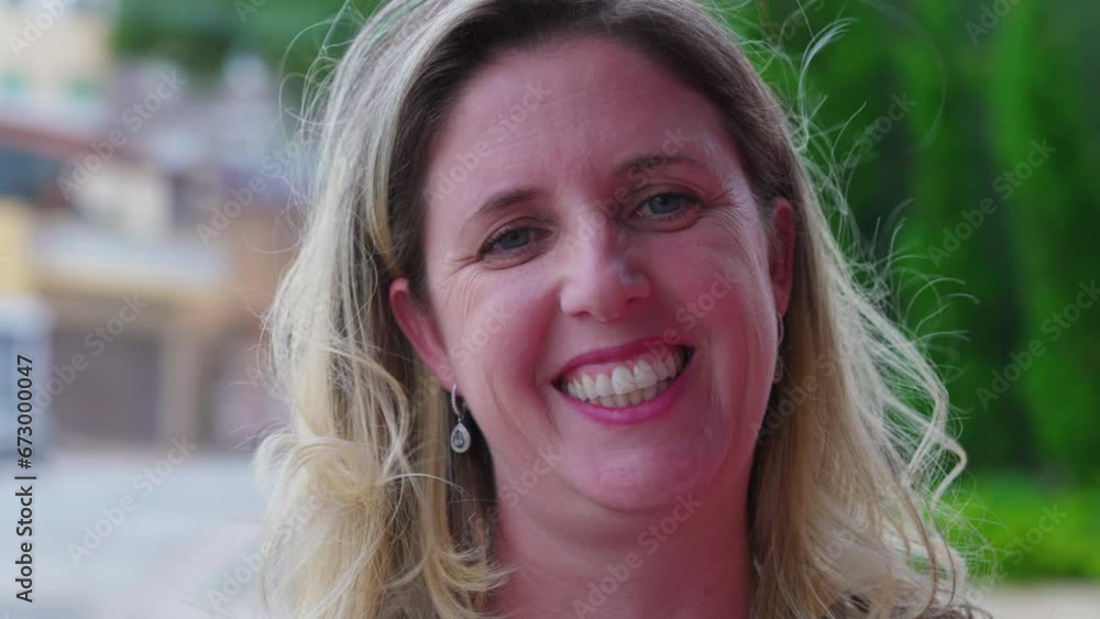 Portrait of a happy woman in 40s smiling at camera standing outside with wind blowing. Close-up face of a joyful female caucasian person Portrait of a happy woman in 40s smiling at camera standing outside with wind blowing. Close-up face of a joyful female caucasian person