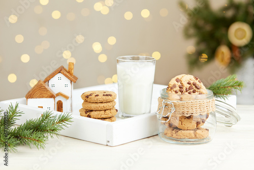 A glass of milk and Christmas cookies for Santa Claus on the table against the background of bokeh lights and a Christmas tree.  photo