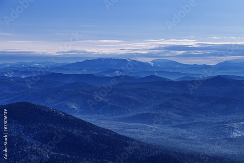 Winter nature panorama of far away blue mountains  picturesque view  aerial tonal perspective  monochrome photo of range mountains and blue sky  hills covered forest  great landscape in Altai
