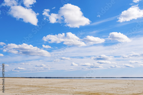 Beautiful shore of lake, white clouds on sky, water surface and sandy beach. Tranquil nature scene, summer sunlight day. Vibrant colored landscape in minimal style, panoramic cloudscape
