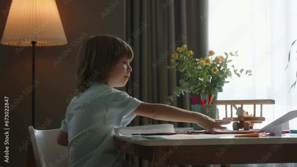 Boy with blond long hair draws against background of window. Cinematic. Child is in wonderful, bright mood, he sings song and dances while sitting on chair. Children development concept, art hobby Boy with blond long hair draws against background of window. Cinematic. Child is in wonderful, bright mood, he sings song and dances while sitting on chair. Children development concept, art hobby