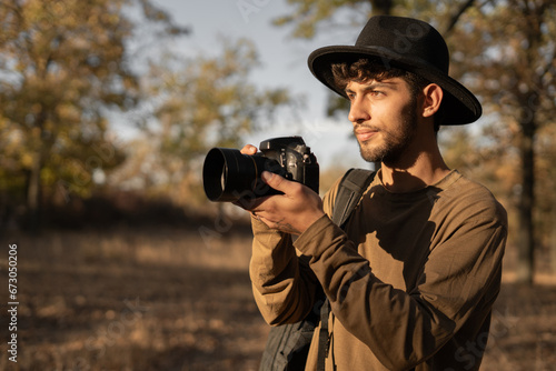 Tableau sur toile Portrait of travel photographer wearing hat with digital camera making photo of the nature at sunset