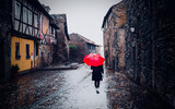 雨の中世の旧市街を散策する赤い傘の女性