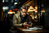Serious businessman in a jacket engrossed in texting on his smartphone at a coffee shop during the evening, symbolizing urban connectivity.