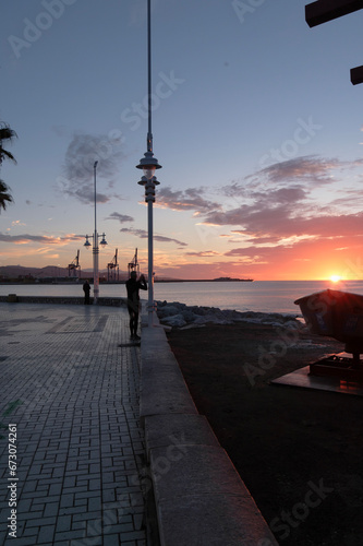 Paseo marítimo de Malaga, amanecer, primeros rayos de sol, al fondo el puerto, personas haciendo fotos a la playa © karlos