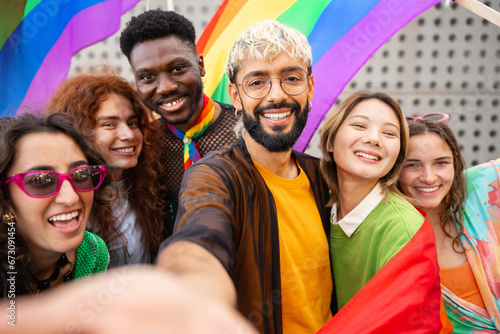 Happy friends taking a selfie photo in the city - Young diverse alternative people having fun with LGBT rainbow flags photo