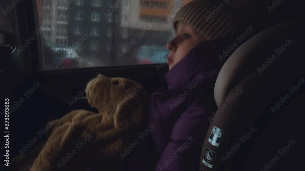 A little girl with a toy in a car child seat, a child with a toy in a car child seat