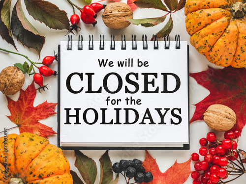 Signboard with the inscription We will be closed for the holidays. Bright pumpkins, tree leaves, red berries and colorful flowers lying on an empty table. Close-up, indoors. Studio shot