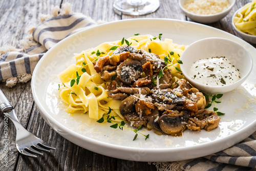 Tagliatelle with roast pork loin, parmesan cheese and mushrooms served on wooden table
