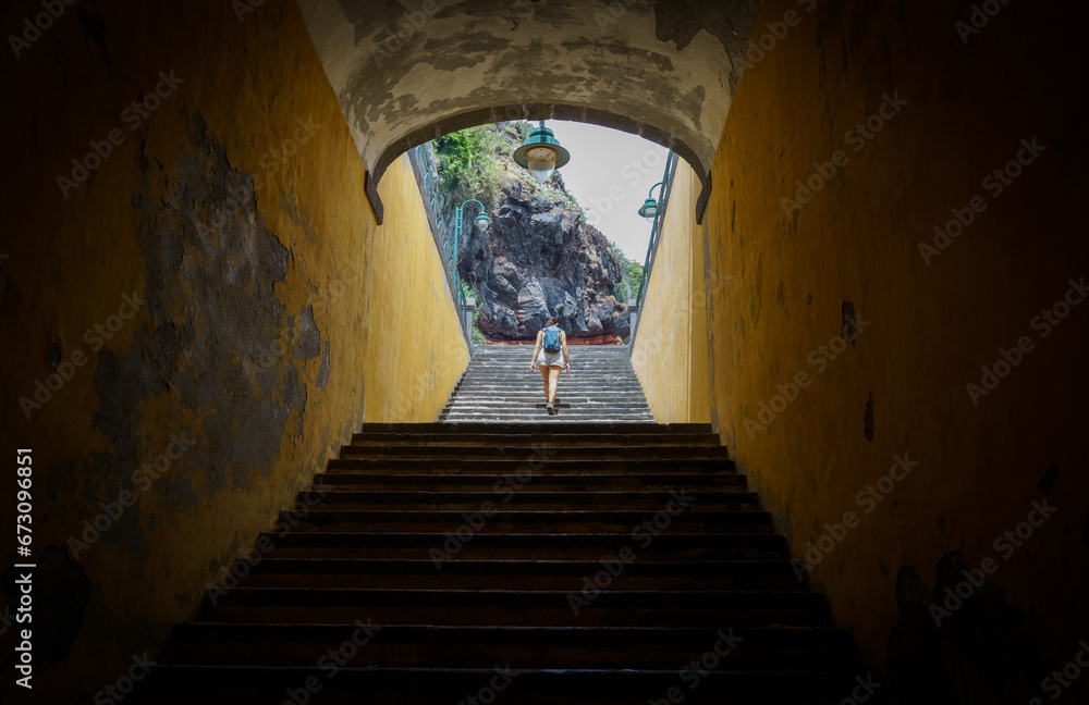 Foto de una chica subiendo unas escaleras en la isla de Madeira con paredes amarillas y roca volcánica al fondo.