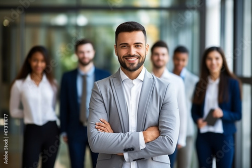 Portrait of handsome smiling businessman with his colleagues  Multi-ethnic group of business persons standing in modern office  Successful team leader and his team in background