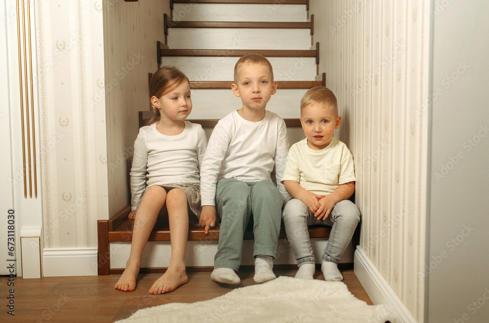 © Ala - two brothers and sister sitting on the stairs in a cozy wooden house