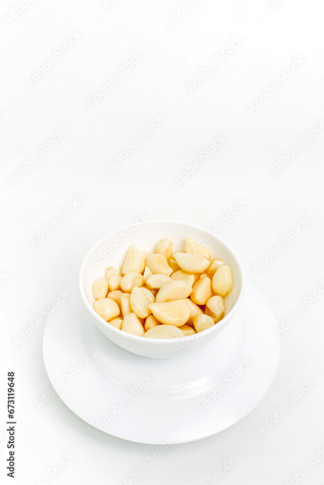 Peeled garlic cloves in a white plate on a white background. Peeled garlic cloves in a white plate on a white background.