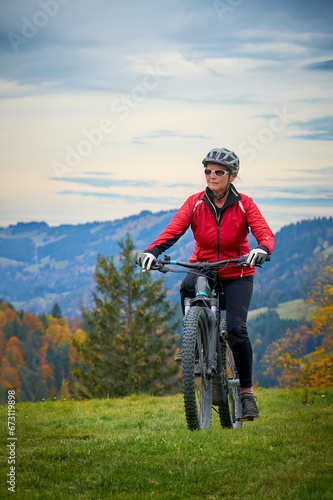 pretty senior woman riding her electric mountain bike in autumn and enjoying the spectacular view over the Allgau and Bregenz Forest alps near Steibis, Bavaria, Germany