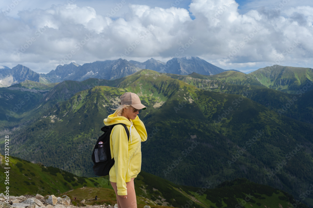 A young girl in a yellow hoodie and cap, a traveler in the Polish Tatras, the sky in the clouds.
