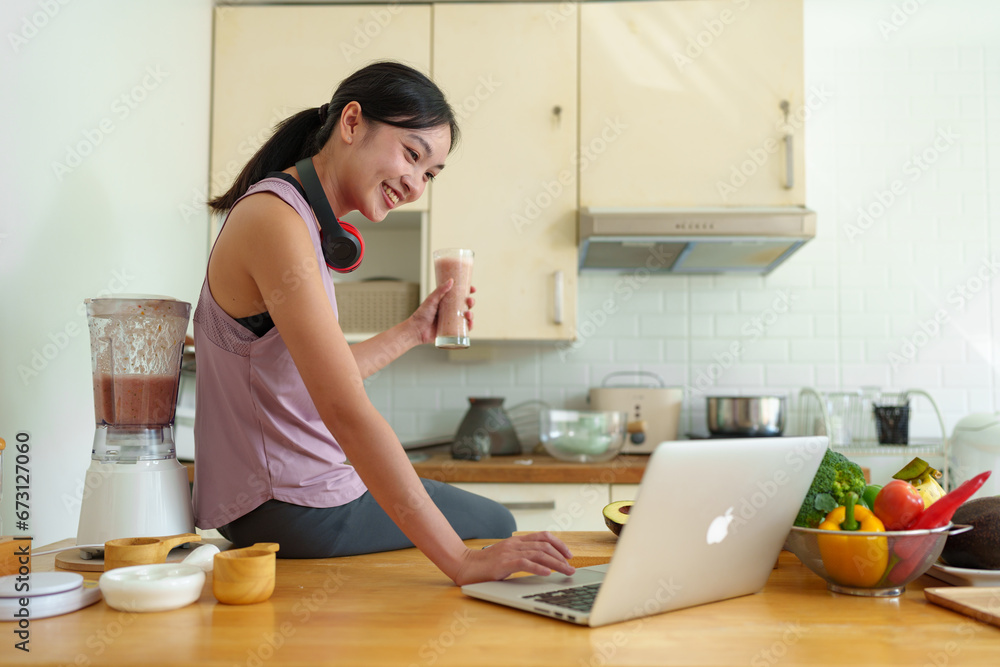 Young woman in Asian exercise clothes making a fruit and vegetable smoothie after a healthy workout at home. Concept of diet and healthy food, lifestyle Young woman in Asian exercise clothes making a fruit and vegetable smoothie after a healthy workout at home. Concept of diet and healthy food, lifestyle