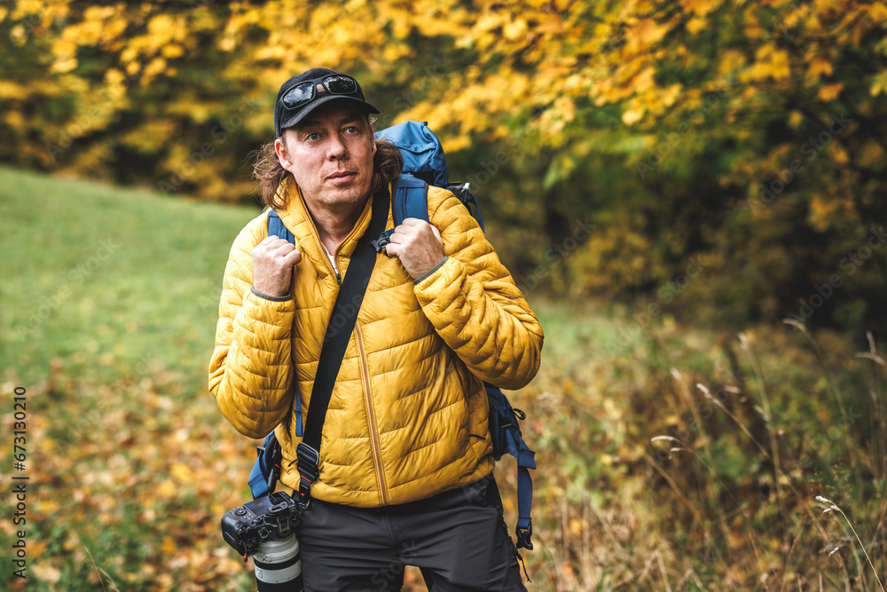 Man with yellow jacket, backpack and camera hiking in autumn woodland. Wildlife photographer exploring forest and bird watching Man with yellow jacket, backpack and camera hiking in autumn woodland. Wildlife photographer exploring forest and bird watching