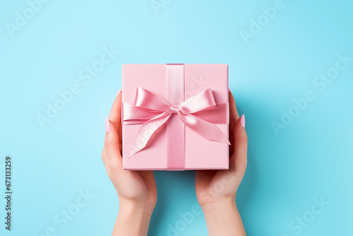 Photo of female hands holding a gift with a ribbon on blue background. Concept of holidays and gifts. AI generated content.