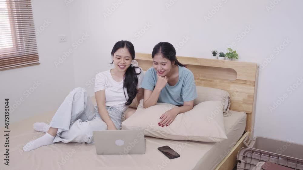 Asian female roommates, students, or schoolgirls use their laptops to work on assignments or review their lessons while seated on the bed and floor within their dormitory Asian female roommates, students, or schoolgirls use their laptops to work on assignments or review their lessons while seated on the bed and floor within their dormitory