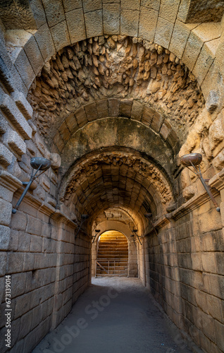 Interior of one of the entrances to the stands and stage of the ancient Roman Theater of M  rida  with a vaulted ceiling of stones and rocks and torches on the walls. Sunlight through the stairs.