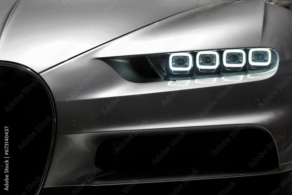 Frontal closeup of modern gray car while the led lamps are on in low light that shows the style and design of the luxury car 