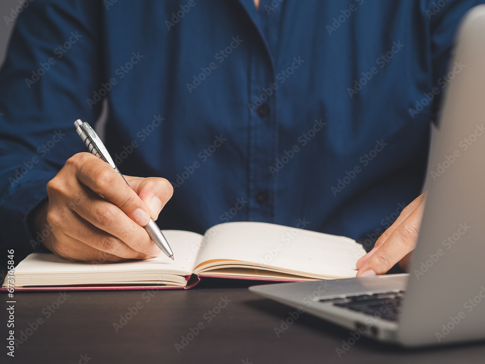 Businessman hand holding a pen and writing in a notebook while sitting in the office Businessman hand holding a pen and writing in a notebook while sitting in the office