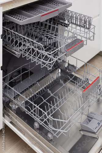 Modern built-in empty dishwasher with open door in the kitchen .