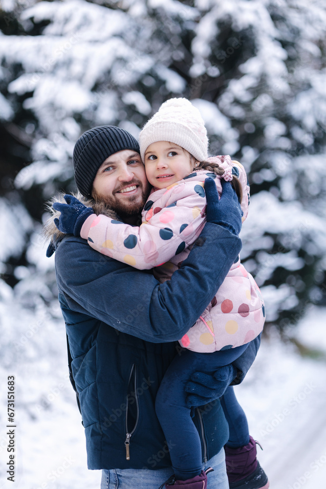 Portrait of happy dad with his beautiful little girl in snowy forest. Happy family time at Christmas holidays 