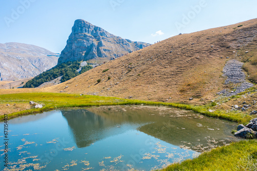 A lake with grass around it and a mountain peak reflected in the water