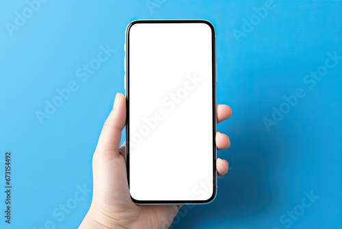 Hand holding smartphone with blank screen on blue background. Mock up