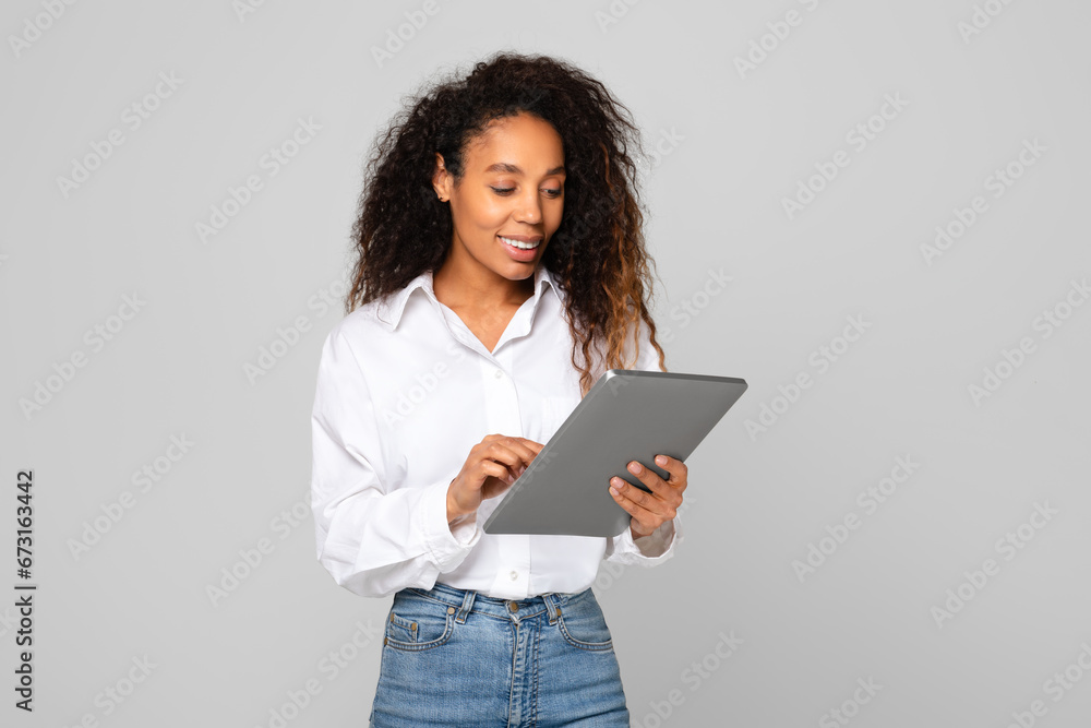 Happy young black woman engaging with digital tablet, gray background Happy young black woman engaging with digital tablet, gray background