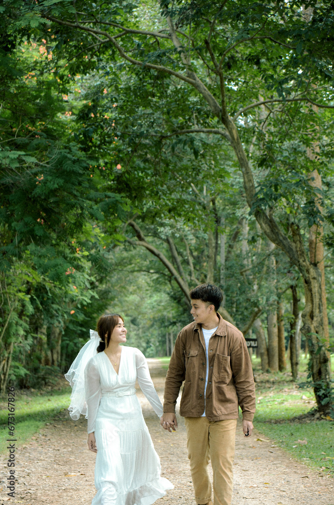 asian couple are walking and holding hand together on road with tree background asian couple are walking and holding hand together on road with tree background