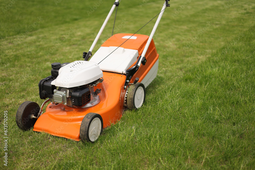 Fototapeta premium Top view of modern orange-grey electric lawn mower cutting bright lush green grass. Gardening work tools. Rotary lawn mower machine on lawn. Professional lawn care service. Place for text