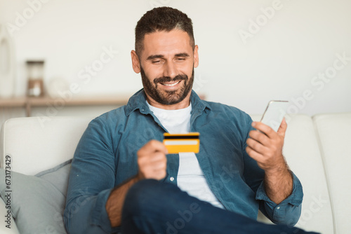 European man holding smartphone and credit card while shopping indoor