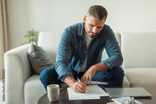 middle aged man signing documents papers sitting on couch indoors