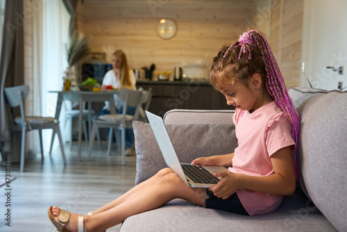 Little girl with braided hair playing laptop sitting on sofa