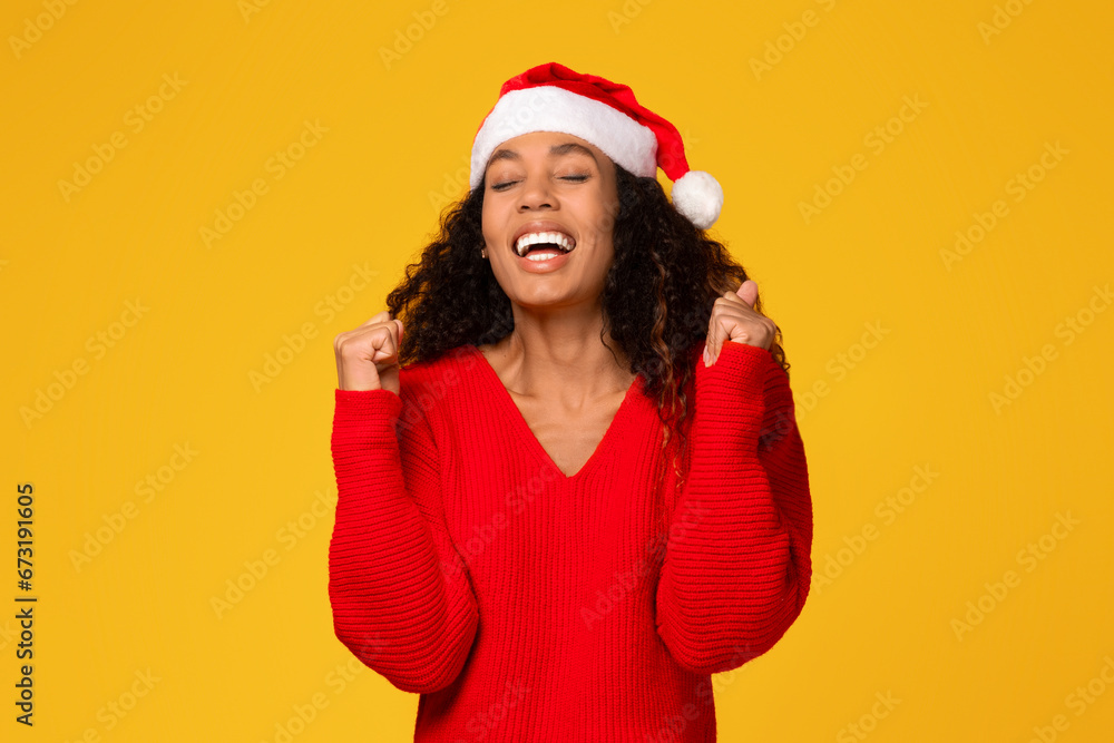 Black woman in Santa hat cheering loudly, clenching fists and screaming yes Black woman in Santa hat cheering loudly, clenching fists and screaming yes