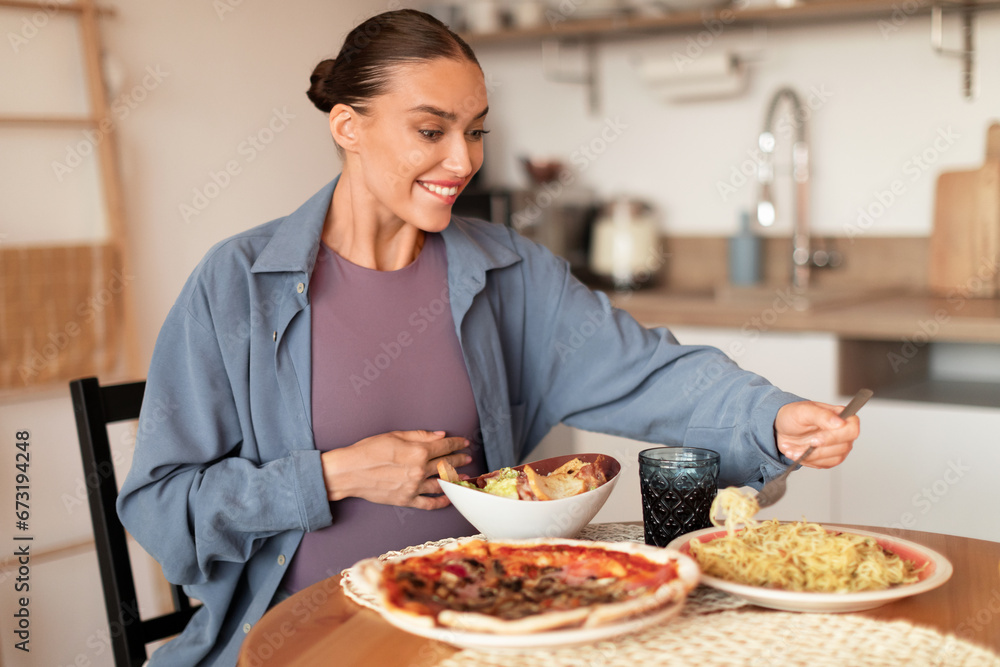 Hungry pregnant woman relishing meal at her cozy kitchen