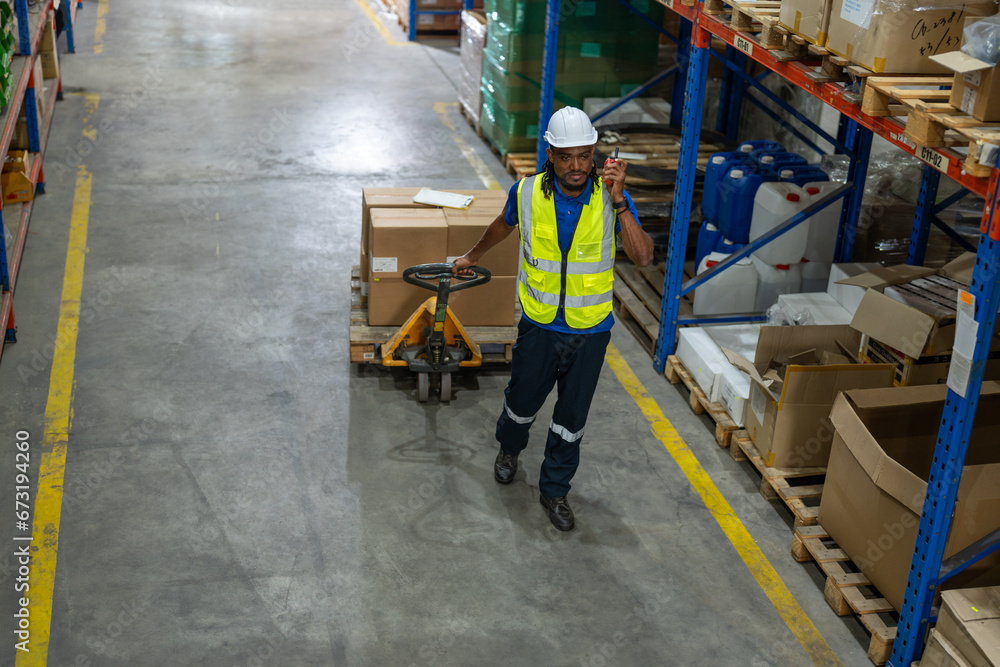 African American man worker using pallet truck for move cardboard boxes. Storehouse employee in uniform working and unloading goods in warehouse. Logistics, Distribution Center concept. African American man worker using pallet truck for move cardboard boxes. Storehouse employee in uniform working and unloading goods in warehouse. Logistics, Distribution Center concept.