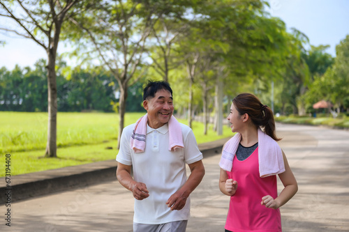 Asian Elderly Father and Daughter are jogging and relaxing in a green park, Breathing in the fresh air and enjoying the beautiful scenery. Health care and family bonding.