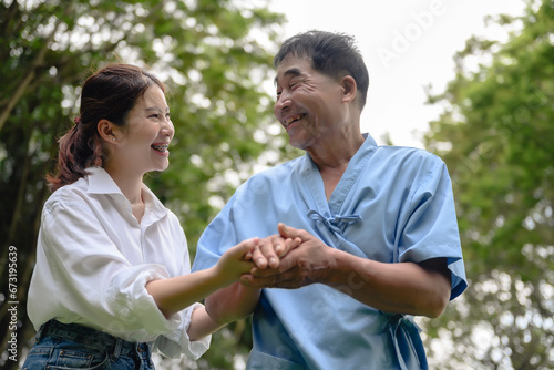 Daughter takes care of father and helps Support, Encourage him during his illness at hospital garden. The happiness of old adult patients while rehabilitation or physical therapy of retired patients. © kokliang1981