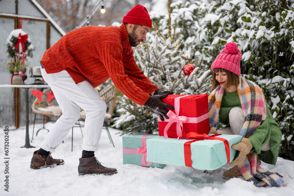 Man and woman put presents under Christmas tree while decorating backyard for a winter holidays. Happy family celebrating New Year's holidays outdoors