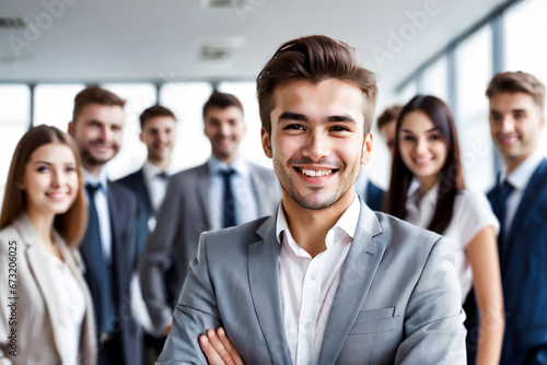 Young smiling businessman standing in front of team, smiling at camera