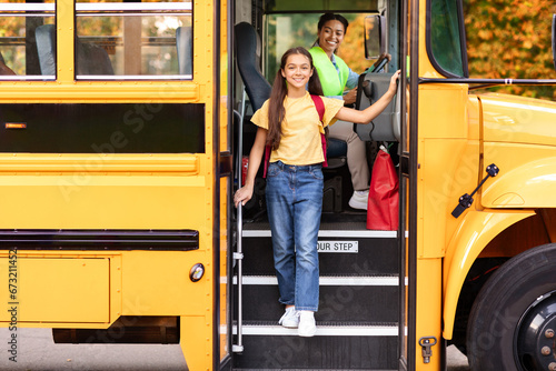 Happy preteen girl getting of the yellow school bus, smiling at camera