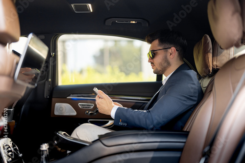 Businessman sits with phone on a backseat of luxury car. Man doing business on the road in prestigious car. Concept of business transportation © rh2010