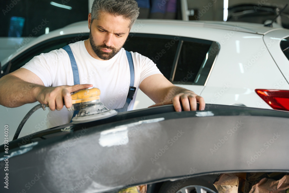 Focused car detailer buffing auto body panel with orbital polisher